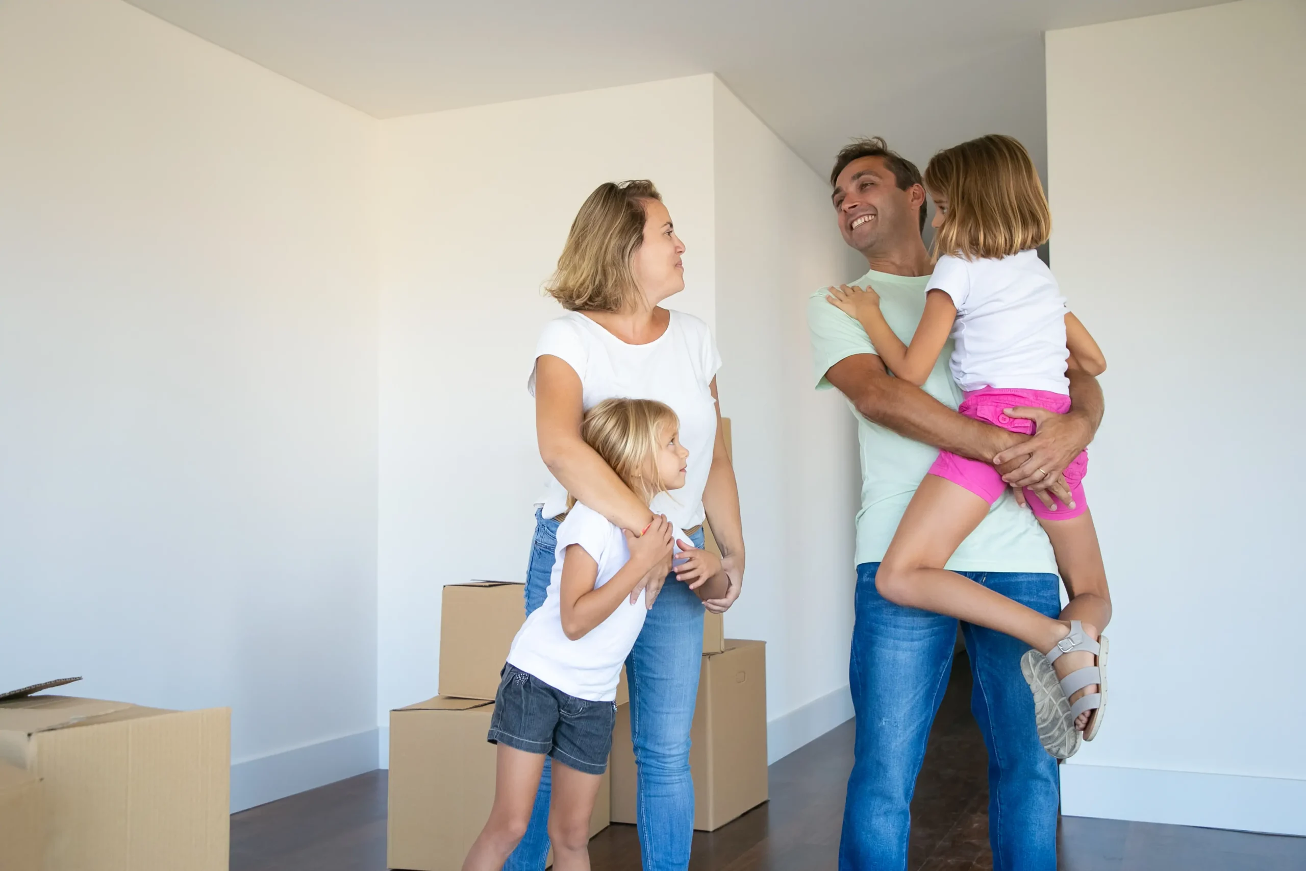 happy-parents-kids-enjoying-moving-into-new-flat-standing-near-stack-boxes-hugging